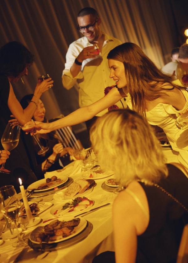 Гости чокаются бокалами за праздничным столом в тёплом вечернем свете